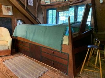 bed next to window with green blanket, and drawers built-in underneath bed