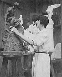 woman in white studio apron works on clay figurative sculpture