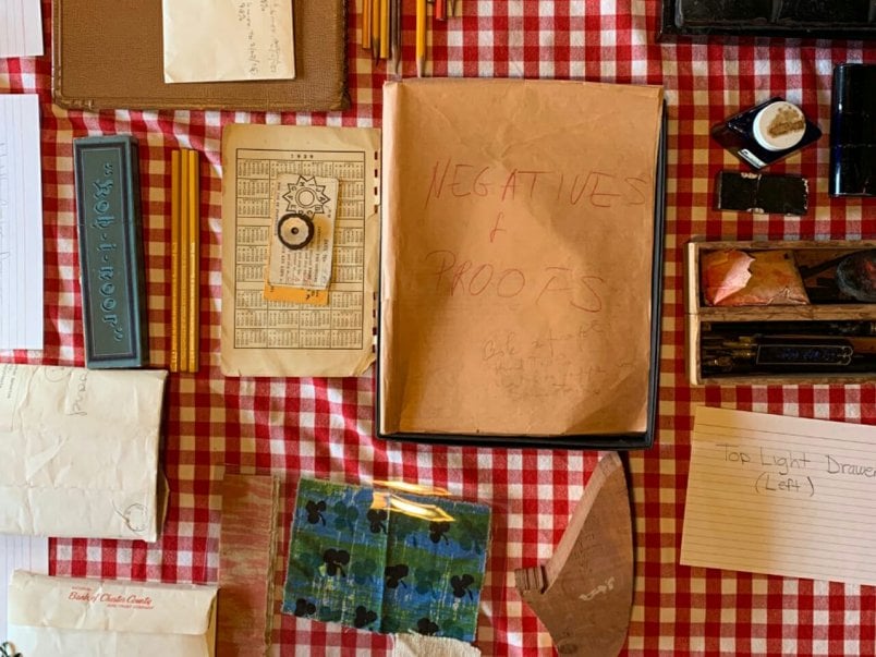 view from above of papers, pencils, ink bottles, envelopes spread out over checkered tablecloth