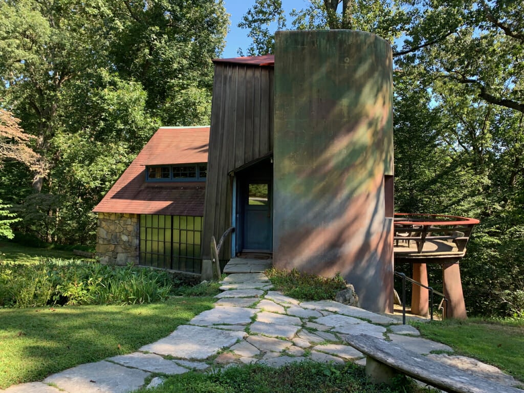 view of studio building with stone section on left and stucco silo on right dappled in shadows from the trees
