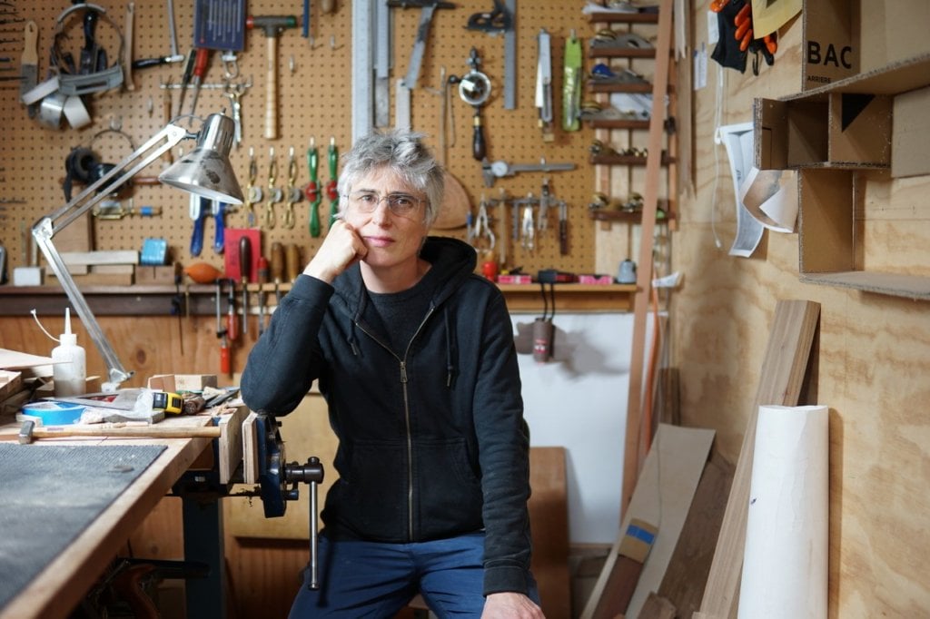 Woman in workshop in front of wall of woodworking tools