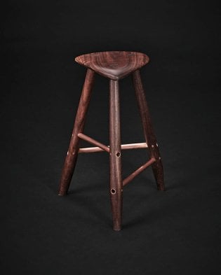 three legged wood stool with copper struts photographed against a black background