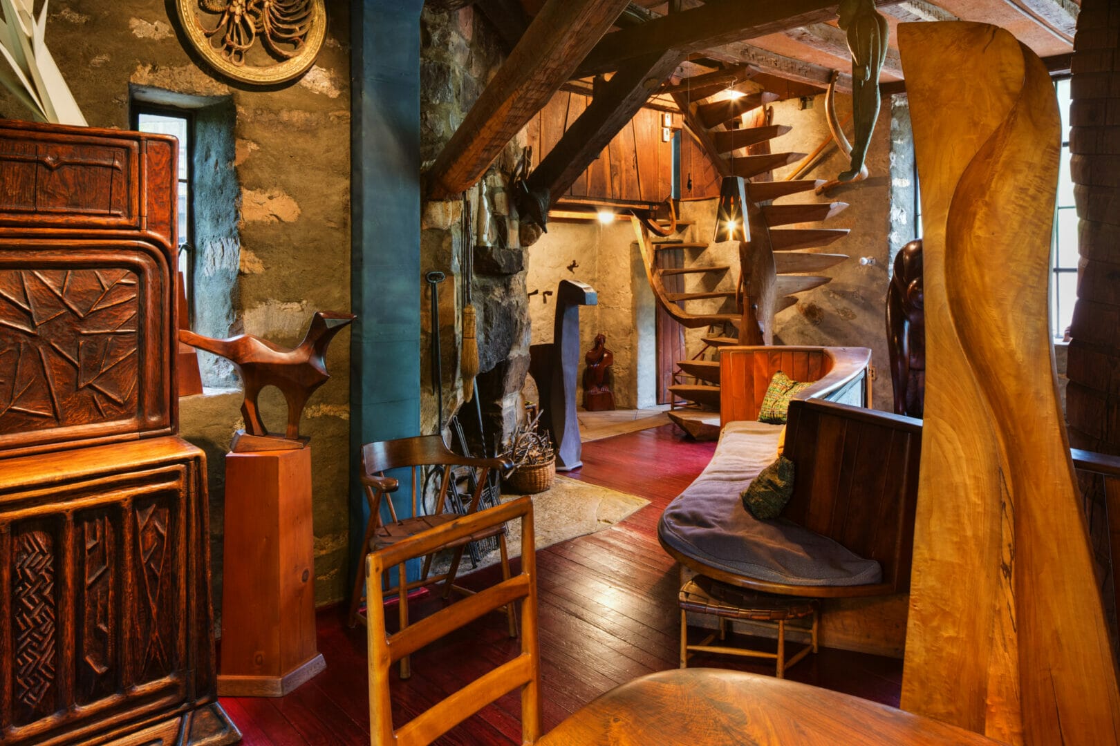 room full of handmade wooden furniture and sculpture, with handmade woden spiral staircase towards the far end of the room.