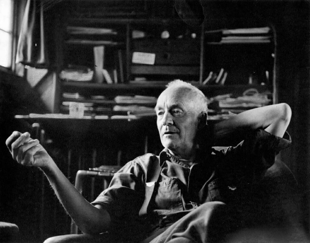 black and white photo of Wharton Esherick seated with his left hand behind his head and his right hand out in front of him, gesturing in conversation