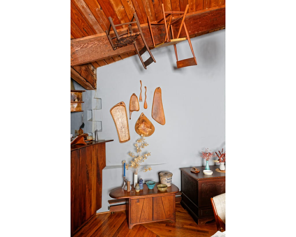 wooden platter and spoons hang on a wall over a wooden chest. Chairs hang from the ceiling.