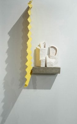 abstract ceramic white forms on a gray shelf next to a yellow vertical zig-zagging divider.