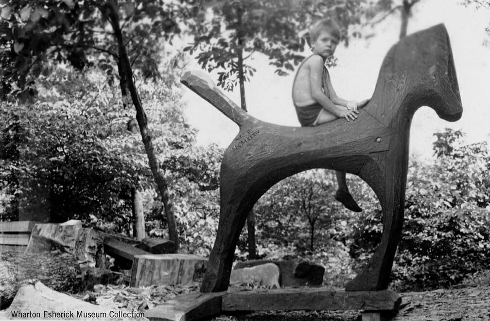 black and white photo of boy on wooden horse sculpture.