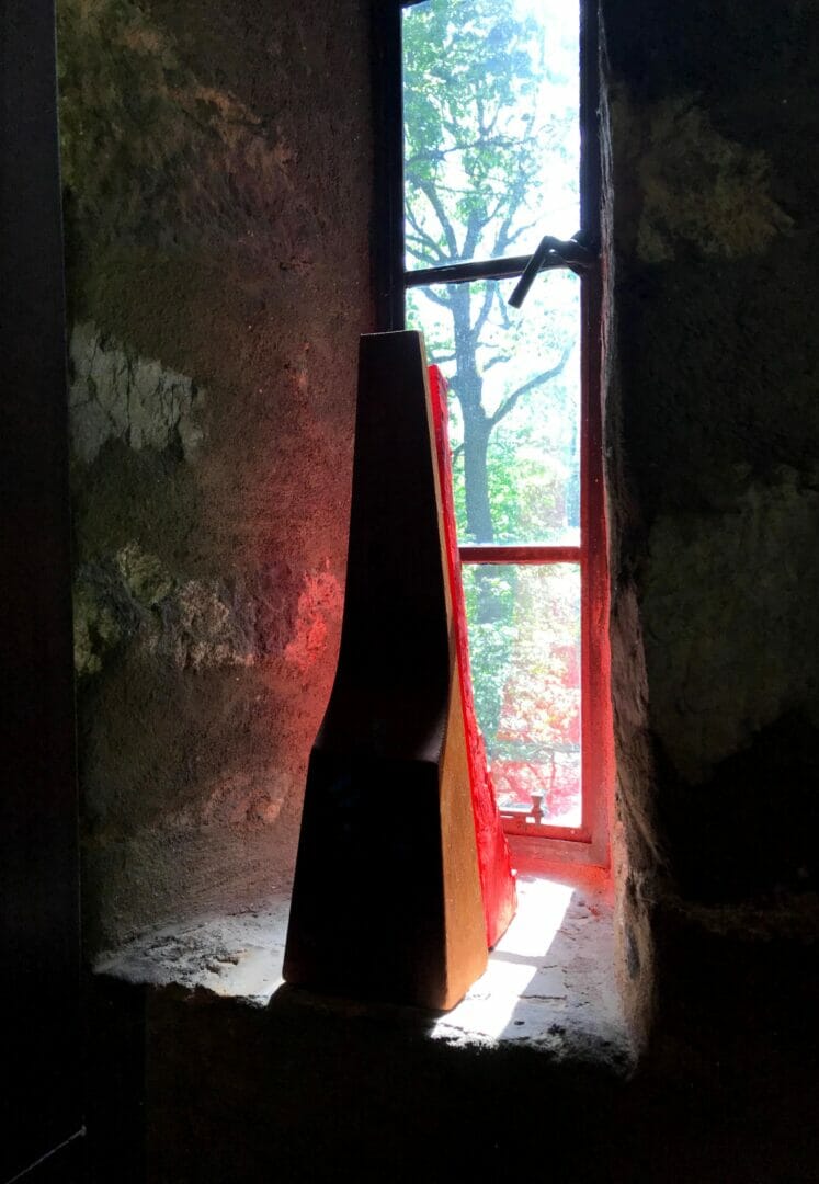 A red sculpture can be seen behind one of Esherick's wood sculptures. Both sit on the sill of a tall, narrow stone window and a red glow reflects around the sculptures.