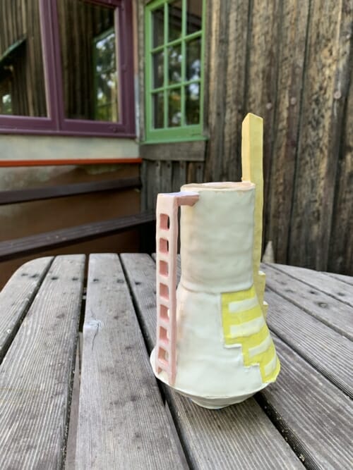 small vase with painted yellow lines, tall yellow "chimney" and pale reddish pink ladder-like handle, on Esherick's deck table