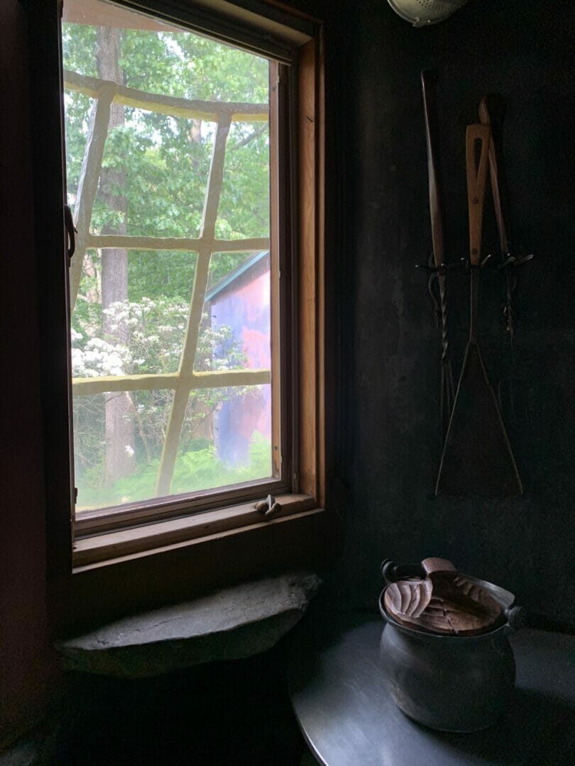 The view from inside the kitchen window shows the grid and a metal pot with a carved wooden lid on a counter in the bottom right of the frame.