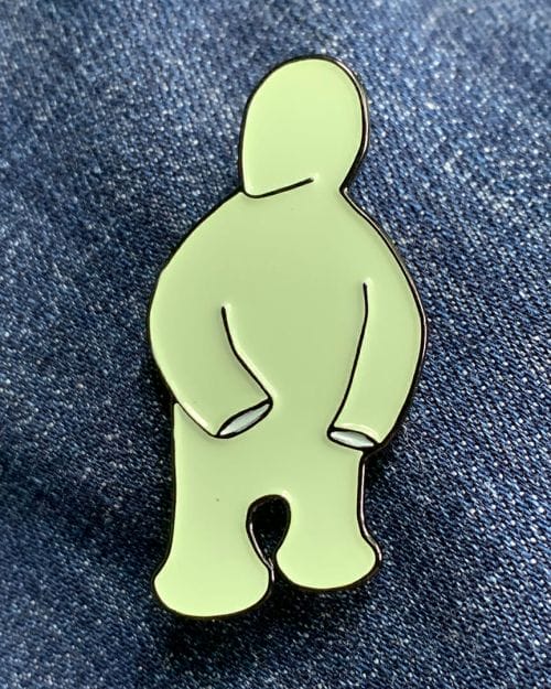 small enamel pin of a cartoonish light green figure on a denim background.