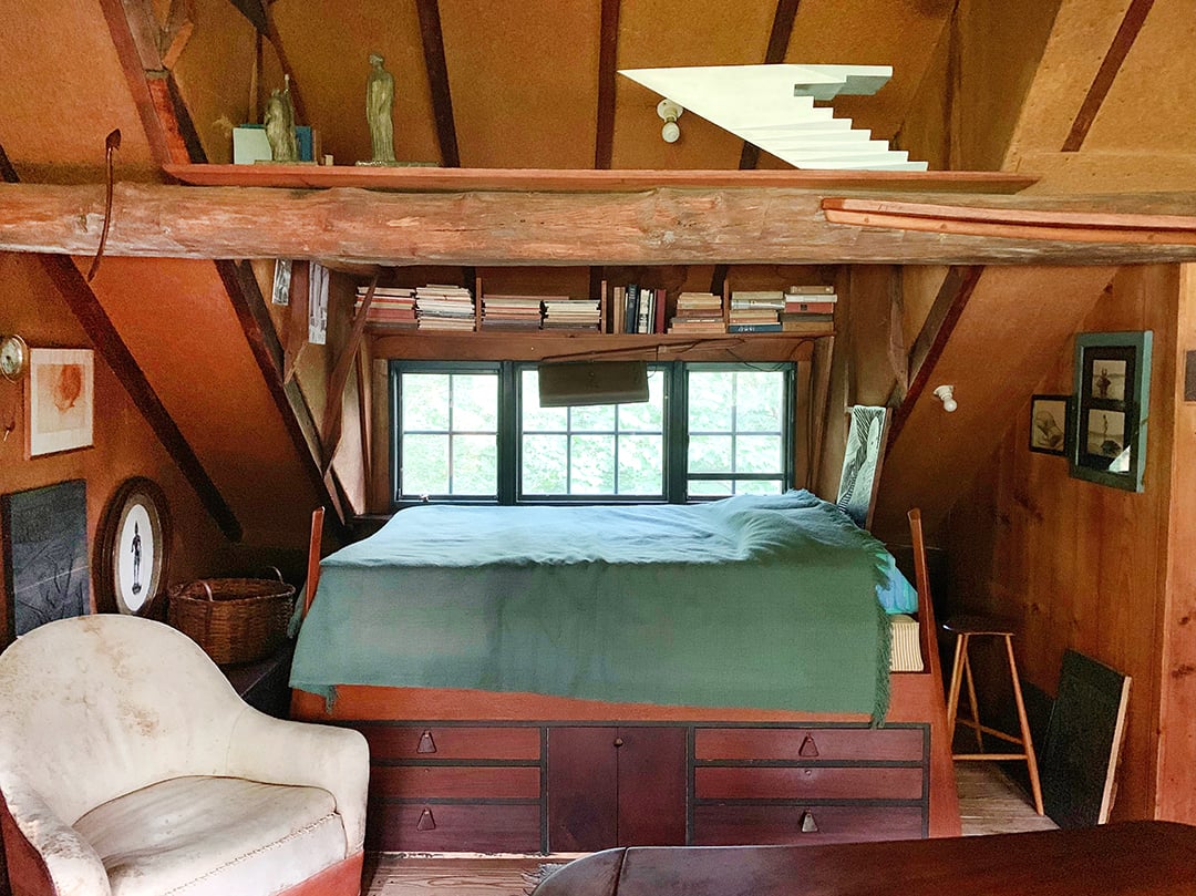 a bed with built in drawers underneath is nestled into an eave and window.