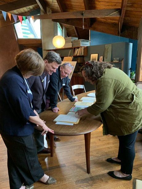 people lean over a curving wooden table to look closely at documents.