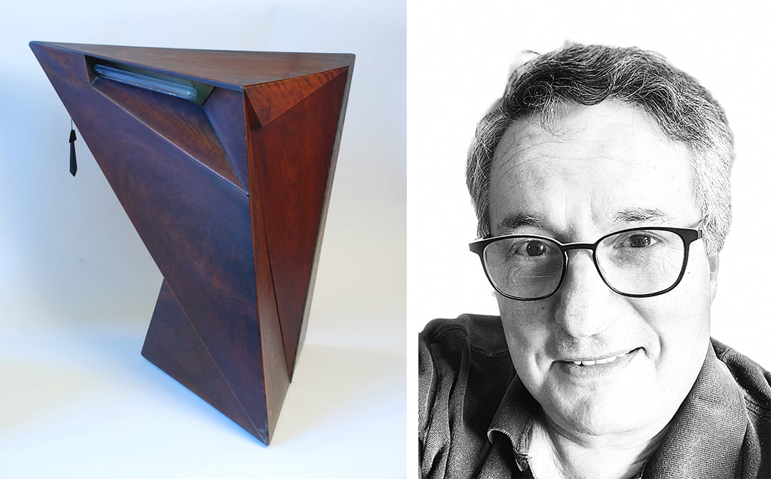 On the left a prismatic, angular wooden end table, on the right is a man with short hair and glasses smiling