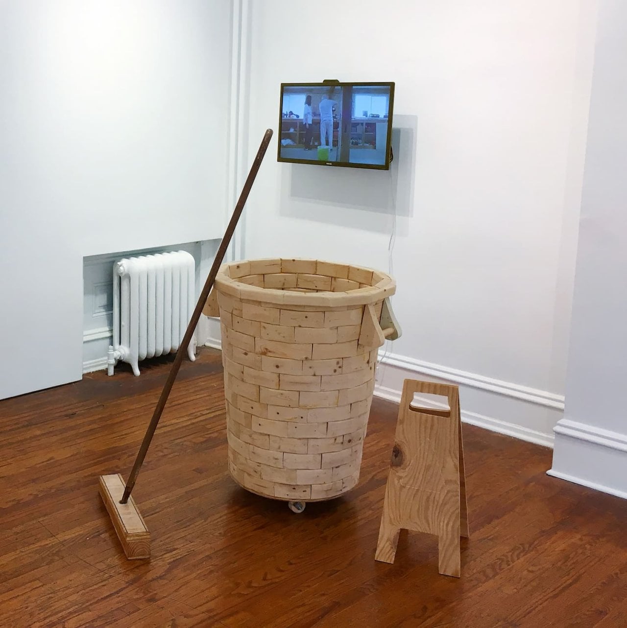 Wooden trash cart, folding sign, and broom arranged in a gallery
